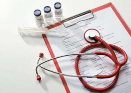Syringe, three vials with clear liquid on top of medical forms on a clipboard – zoomed out