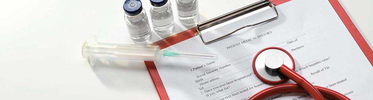 Syringe, three vials with clear liquid on top of medical forms on a clipboard – close up