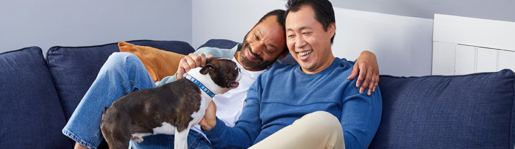 Black male and Asian male sitting on a couch with a dog