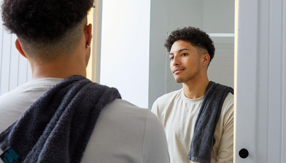 Bi-racial young man looking at reflection in mirror in bathroom