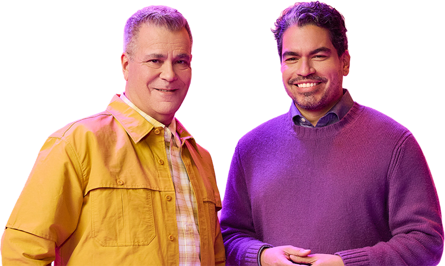 A white male in his fifties and latino man in his thirties smile at the camera, appearing relaxed and happy
