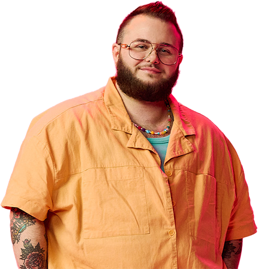 A heavy-set man with tattoos, glasses, and a beard smiles while wearing an yellow shirt and pants against a vibrant pink background, creating a cheerful mood.