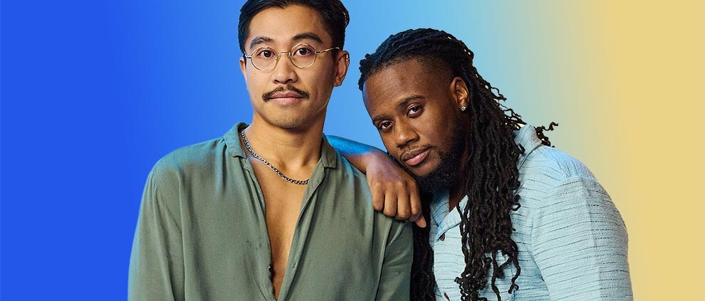 An Asian male and black male against a vibrant blue and yellow gradient backdrop. One leans on the other's shoulder, both projecting a calm, relaxed vibe.
