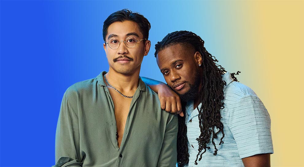 An Asian male and black male against a vibrant blue and yellow gradient backdrop. One leans on the other's shoulder, both projecting a calm, relaxed vibe.