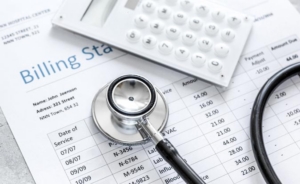 A stethoscope rests on a medical billing statement with a white calculator nearby. The image conveys the concept of healthcare expenses and financial calculations.